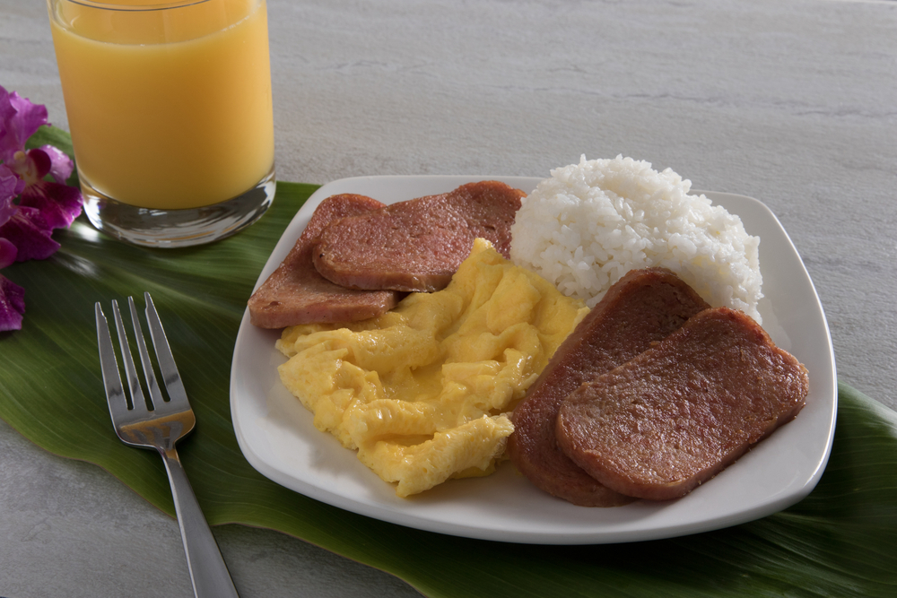 Hawaiian breakfast plate with eggs, Spam, and rice next to a glass of orange juice, popular for Hawaiians to eat