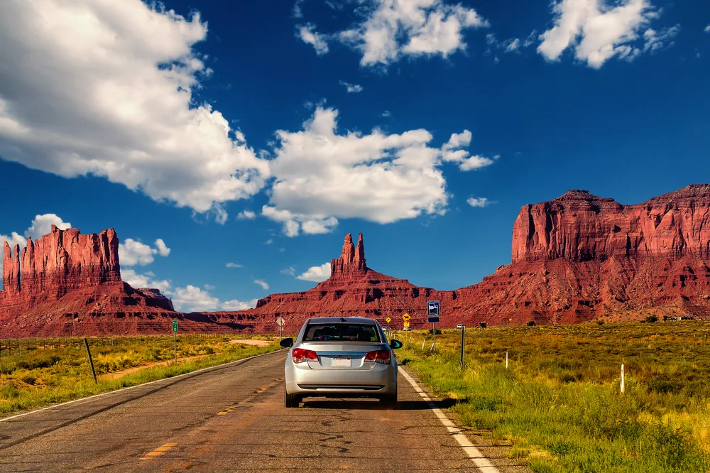 A car driving on a highway towards unique landscapes with red soil. 