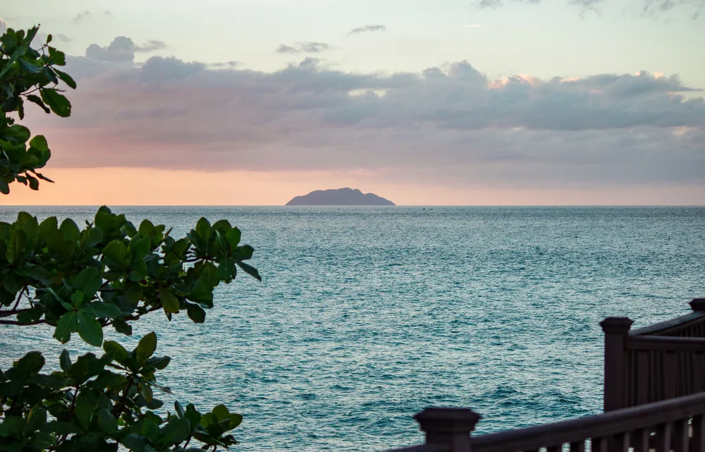 A view from the coast where a small island can be seen from a distance during sunset.