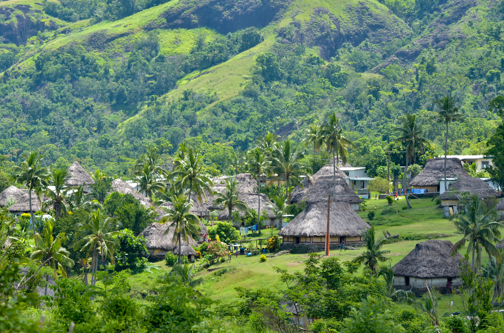 Aerial shot of Navala Village in Viti Levu, Fiji with huts and lush greenery amid the hilly terrain for a post asking how long are flights to Fiji