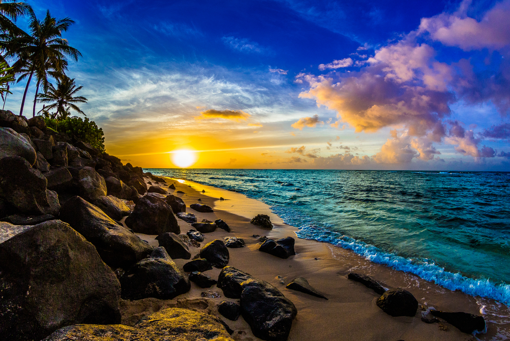 Sunset on the North Shore of Oahu in Hawaii with rocks along the beach and waves gently crashing on the sand, a great summer vacation idea 