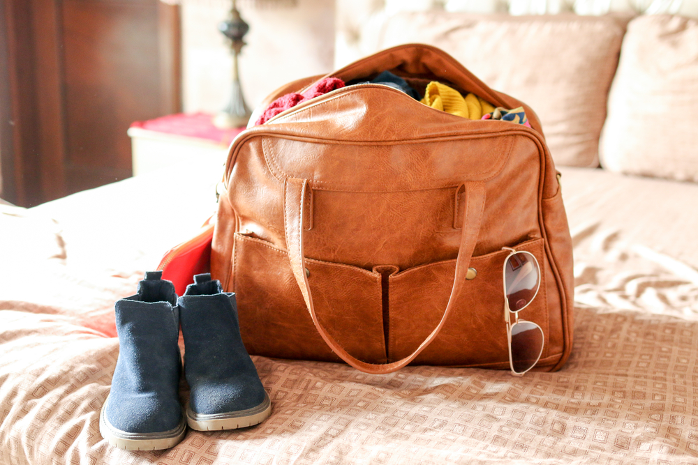 A leather hand bag with shades and a boots placed on the bed.