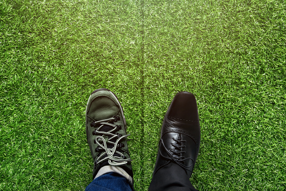 Visual concept of work-life balance shown with a casual shoe on the grass next to a dress shoe as seen from above for an article describing bleisure in business travel