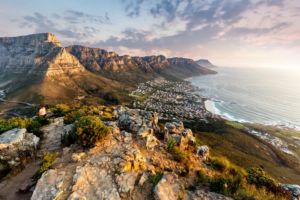 Aerial view of a coastal area in Cape Town, a must visit and one of the best areas to stay in South Africa, a volume of residential houses stands in between row of tall rocky mountains and the sea. 