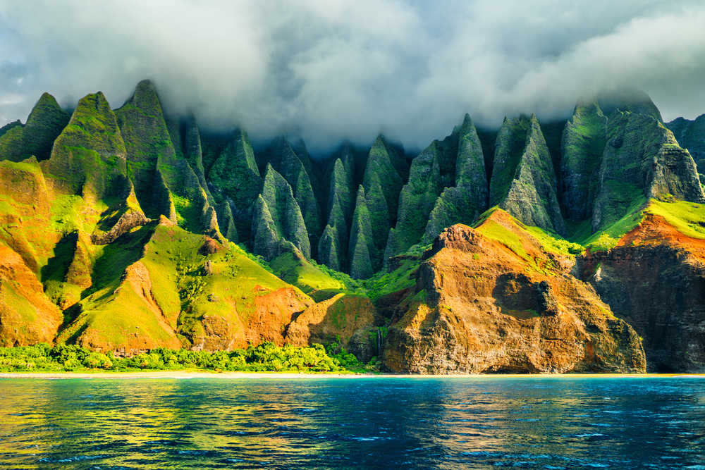 The Na Pali Coast of Kauai seen with morning fog on the mountains during a beautiful day with calm water for a frequently asked questions section on how to move to Hawaii in 7 steps