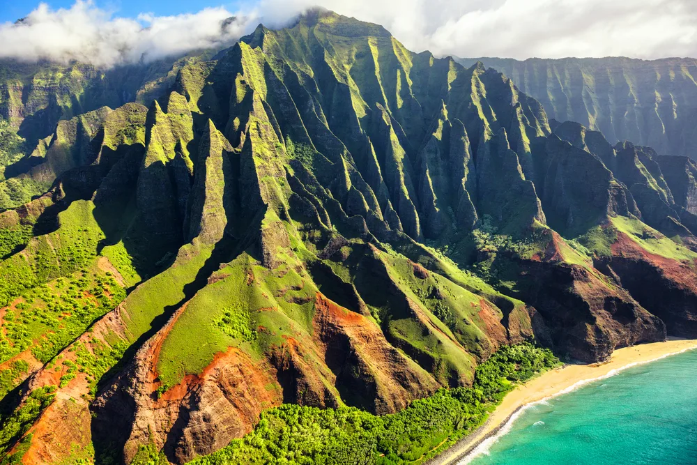 Aerial view of the rugged and green Napali Coast on Kauai, Hawaii on a beautiful day as we explore which airlines fly to Hawaii 