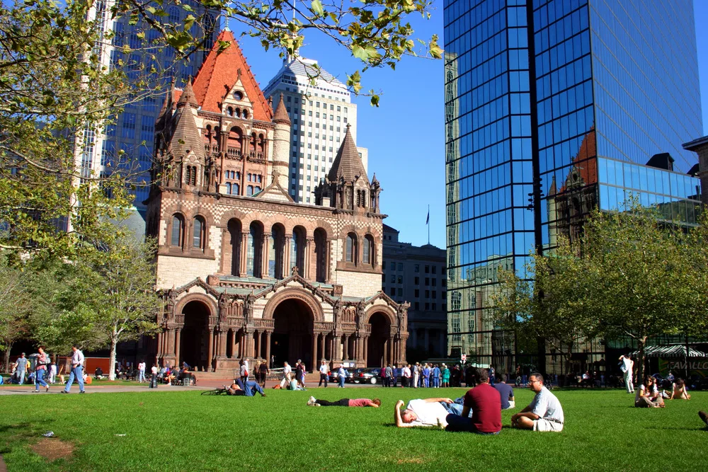 People enjoying the open green field in front of an old structure surrounded by modern buildings during the best time to visit Boston.