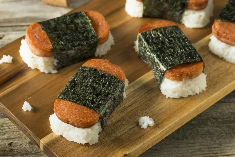 Three pieces of SPAM musubi resting on a wooden cutting board for a guide showing why is SPAM so popular in Hawaii