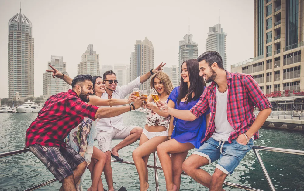 A group of friends partying and drinking on a yacht while buildings can be seen in background.
