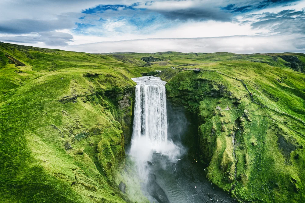 Stunning aerial view of the Skogafoss waterfall in Southern Iceland on a summer day surrounded by greenery for a guide showing the average flight time to Iceland