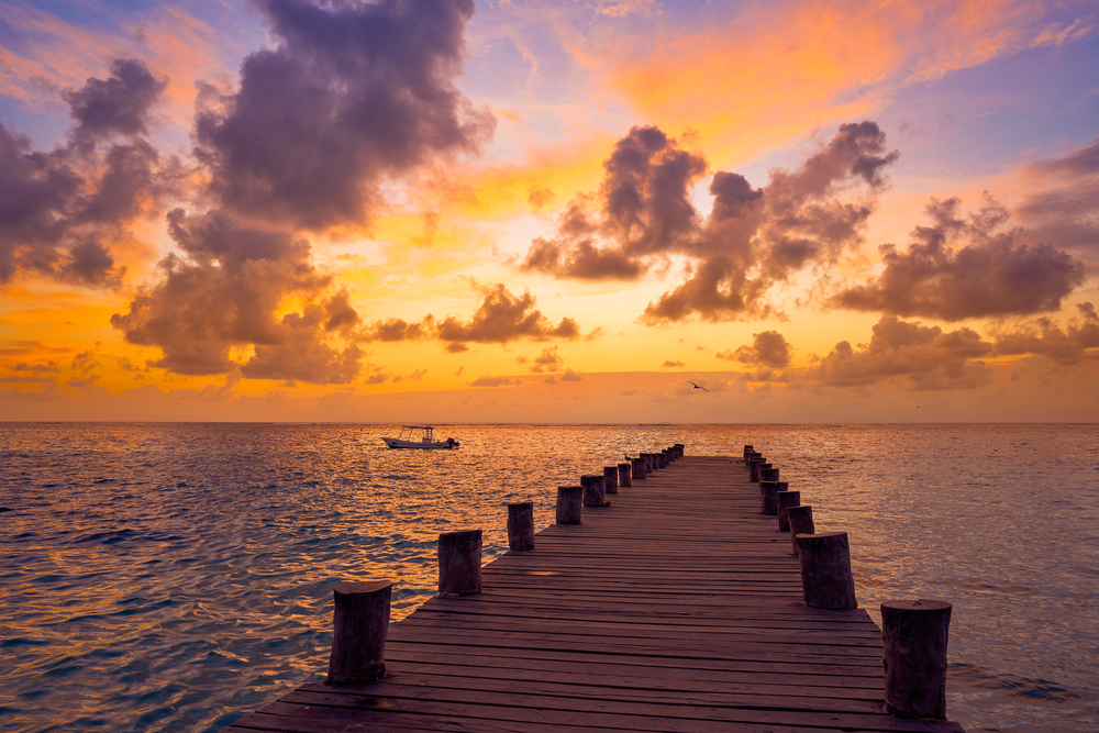 Sunrise at a pier in Riviera Maya with clouds in the colorful sky for a frequently asked questions section asking how long is a Cancun flight from different US cities?