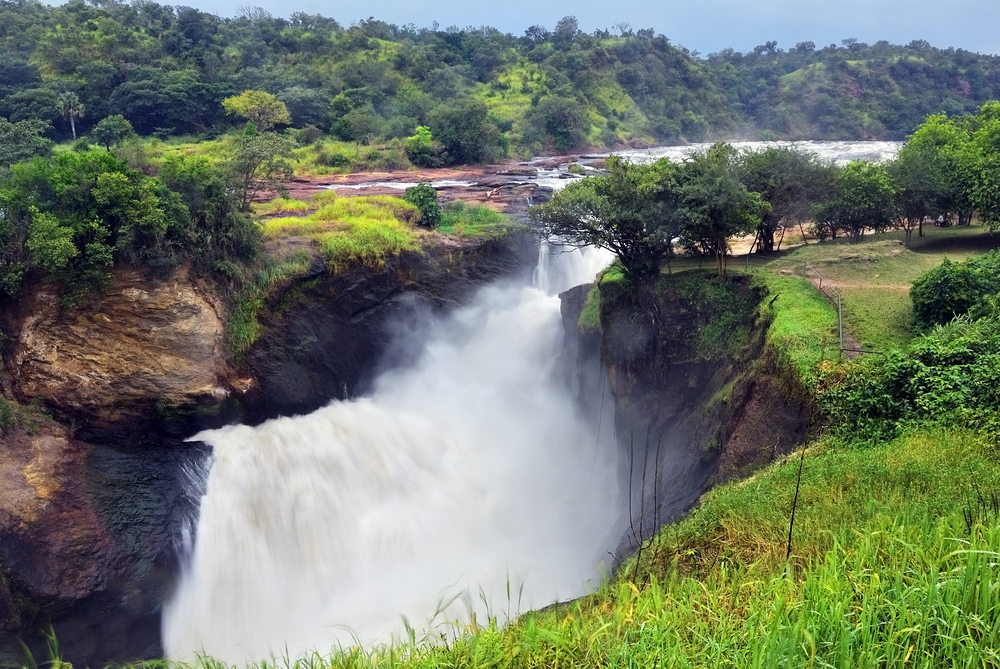 A large gushing waterfalls in Murchison Falls National Park, one of the best areas to stay in Uganda, and on the side are surrounded by trees.