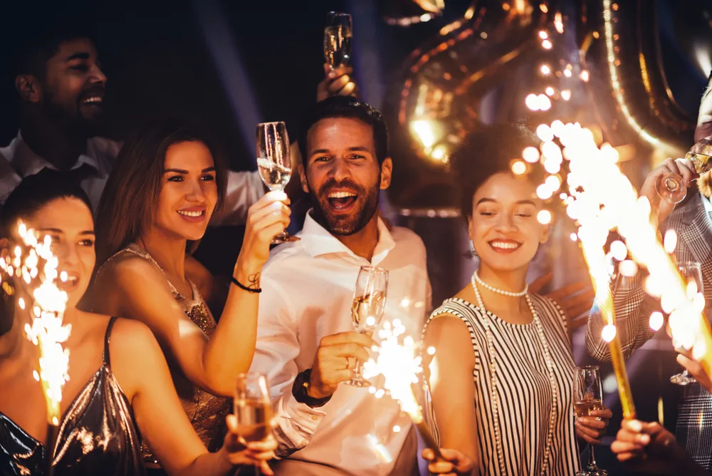 Group of friends smiling with sparklers and champagne at a New Year's Eve party in one of the best places to spend New Years in the USA