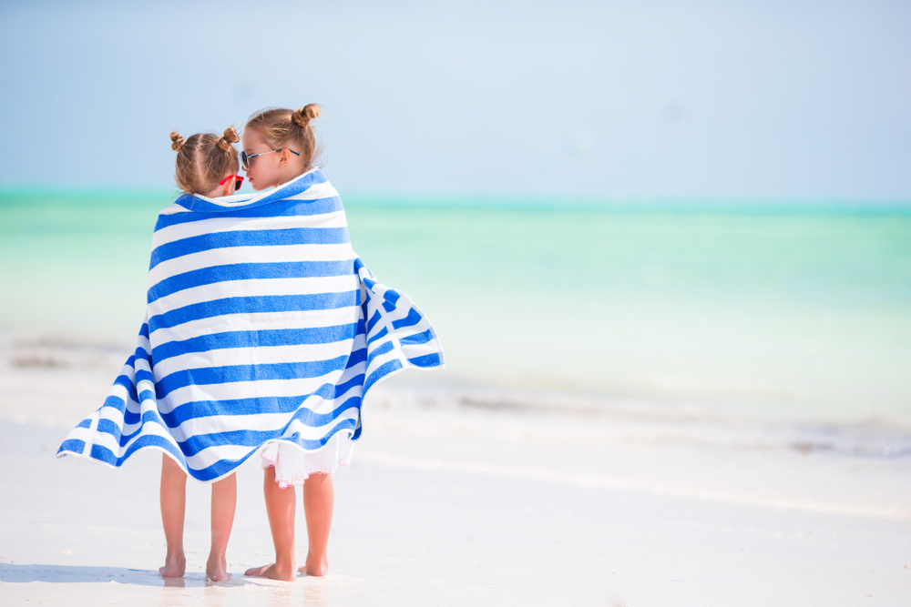 A little girls sharing a towel on the beach. 