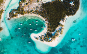 Top view of an island with white sand, where boats can be seen near its shore.