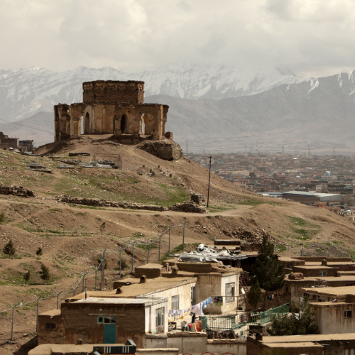ruins of an old structure seated on top of a hill, mountains and a town can be seen in background, during the best time to visit Afghanistan.