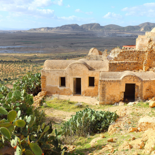 ruins of a house in a desert where mountains can be seen in background and cacti are flourishing during the best time to visit Tunisia.