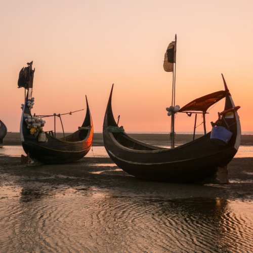 traditional fishing boats on the sand during a low time of a sunset on the best time to visit Bangladesh.
