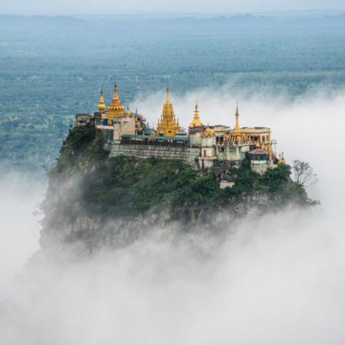 a temple built on top of a mountain peaking above the clouds during the best to visit Myanmar.