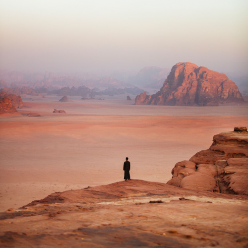 a person standing on the edge of a rock while looking at the hazy desert expanse during the best time to visit Jordan.