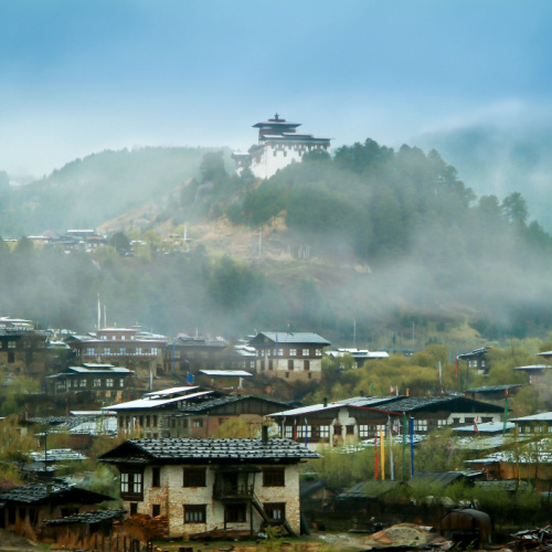 a foggy morning during the best time to visit Bhutan in a small town in a country where a temple can be seen at the top of a hill.