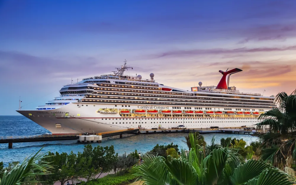 The Carnival Conquest cruise ship of the Carnival cruises docked on a port in the Caribbean during a sunset, an image for the guide on the cost of cruise in the area.