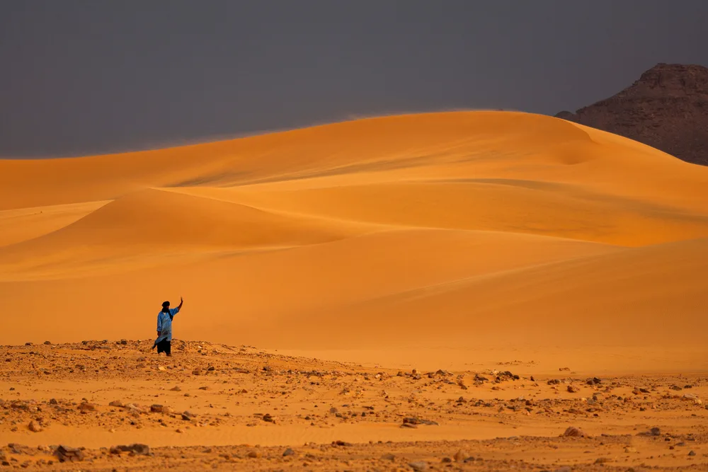 Tuareg and sand dunes pictured with beige sand and a man waving at the camera for a post titled Best Time to Visit Chad