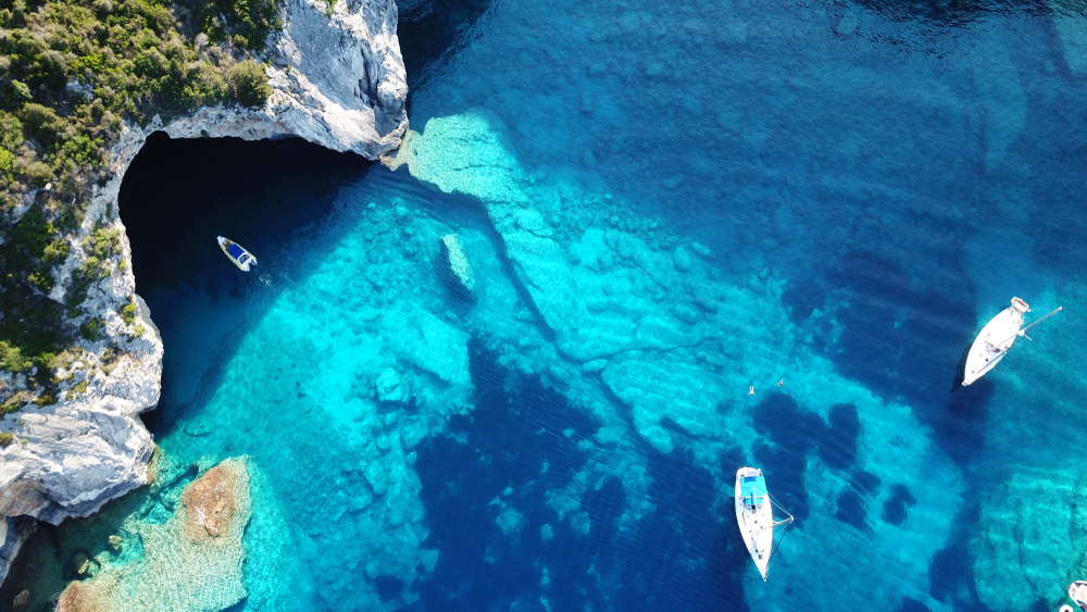 Top view of a remote coast in one of the best Caribbean islands to visit with clear teal waters, a boat can be seen entering a cave. 