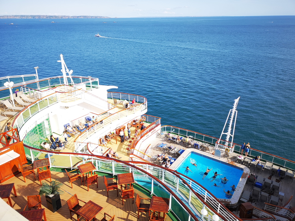 A view from a cruise where people can be seen sunbathing and others are in the pool while the ship is in the middle of the sea, a piece on the guide on cost of Caribbean cruise.