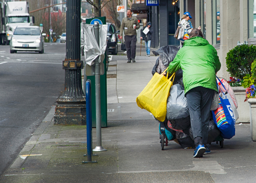 Homeless woman in Portland Oregon pushing her cart along the downtown sidewalk while wearing a green jacket