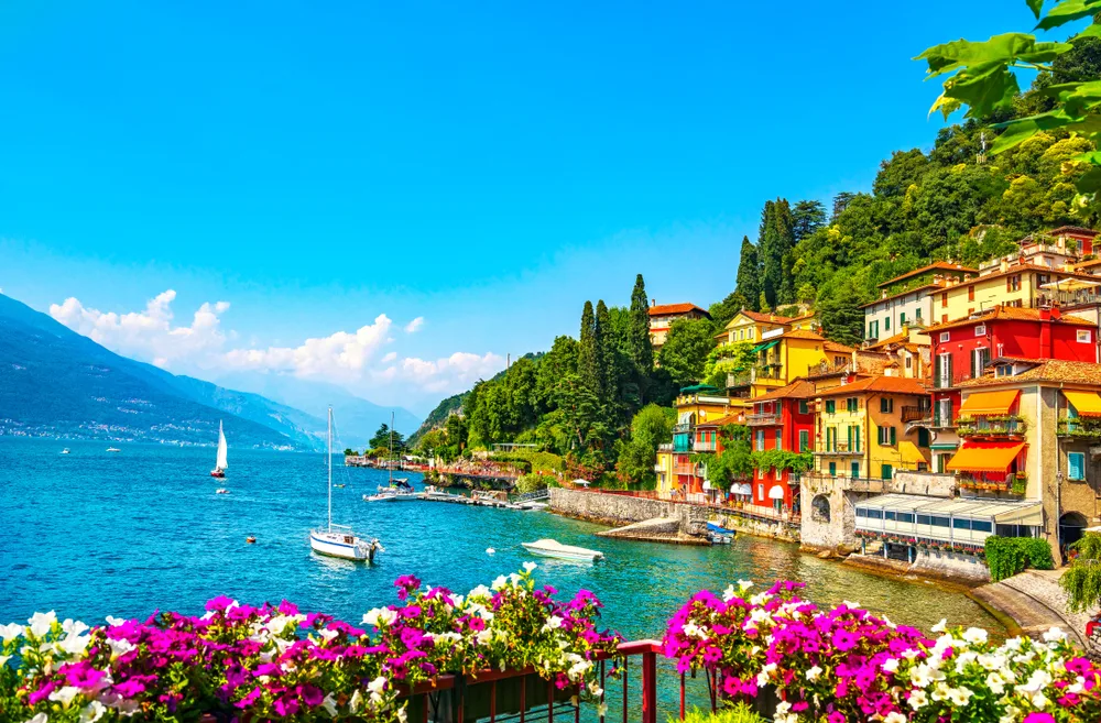 Varenna on the shores of Lake Como with pink flowers blooming and colorful homes showing why it's one of the best cities in Italy you can visit
