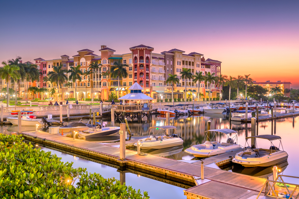 Corner shot of the pier with small boats docked on still water below high-rise condos at dusk for a post on whether or not Naples, Florida is safe to visit