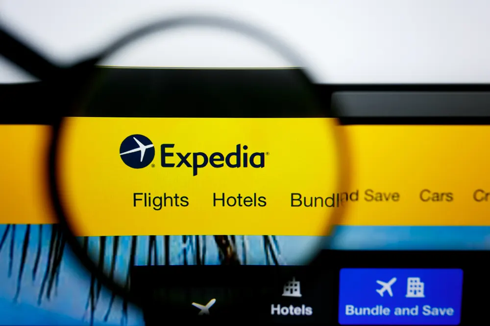 Laptop screen with magnifying glass over the Expedia logo showing flights and hotels for a comparison guide of Booking.com vs Expedia