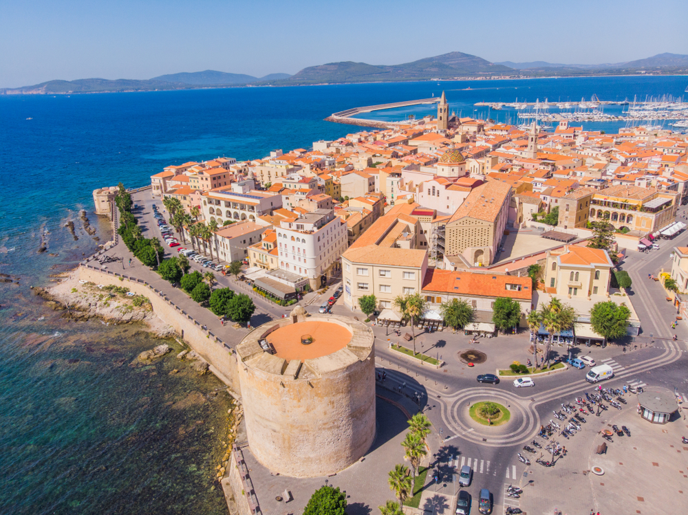 Aerial view of Alghero Old Town on the island of Sardinia, Italy with mountains in the background during a clear day 