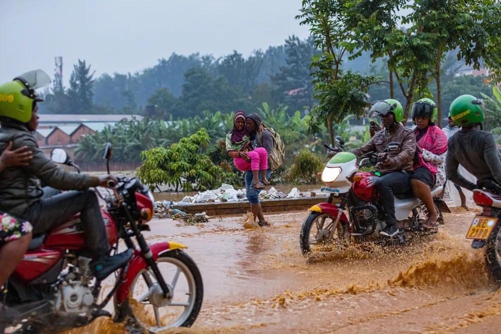 People walking and riding motorbikes driving through a flooded and muddy street for a guide to whether it's safe to visit Rwanda