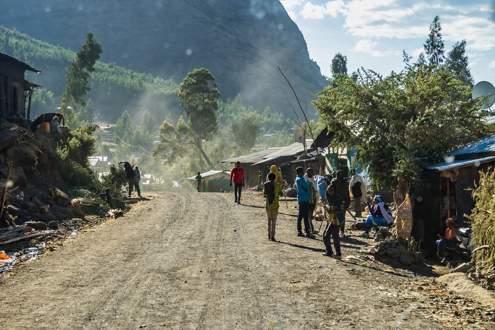 Locals walking along a dirt road at the base of a mountain with shacks set up on either side in Tigray for a guide titled Is Ethiopia Safe to Visit