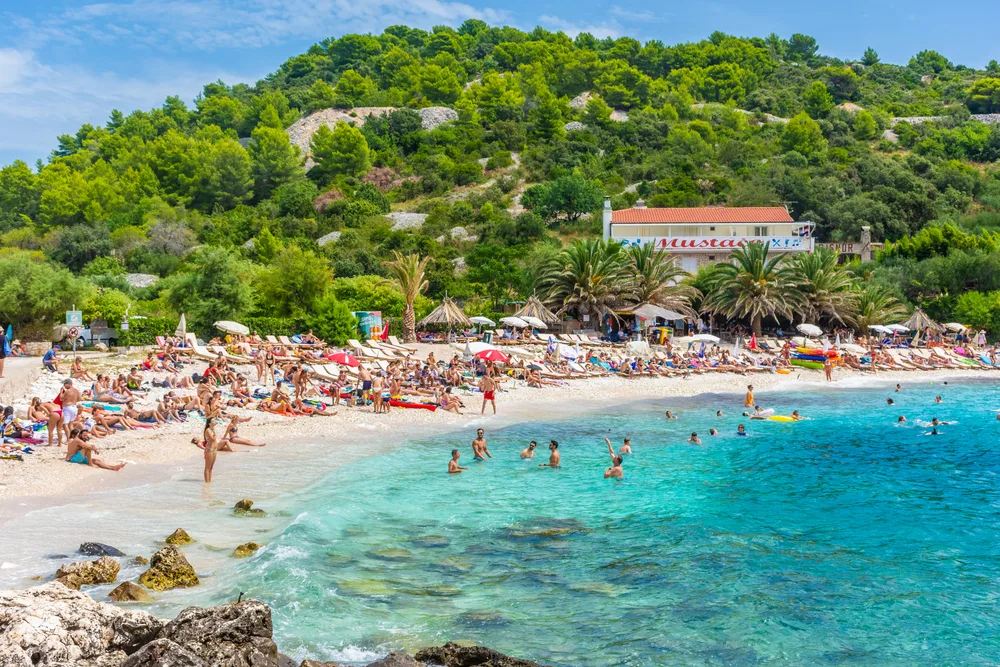 Crowds of people on a picturesque crescent-shaped beach in Hvar, Croatia, for a guide titled Is Croatia Safe to Visit