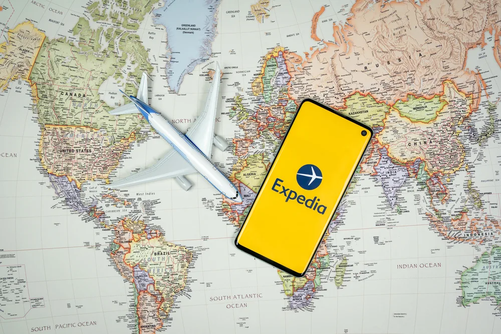 Smartphone showing the Expedia app logo next to a model airplane on a world map to indicate the concept of trip inspiration using travel apps