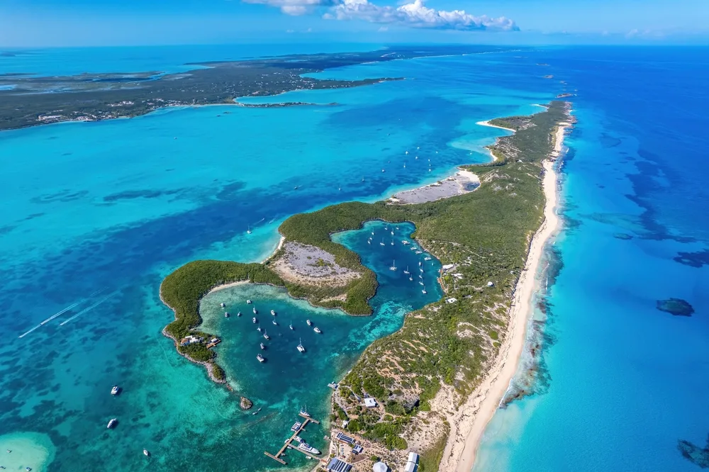 Aerial view of an island where most of its land area is covered with trees, and several boats are anchored on its clear blue waters, an image for a guide on how to get to Exuma Bahamas.