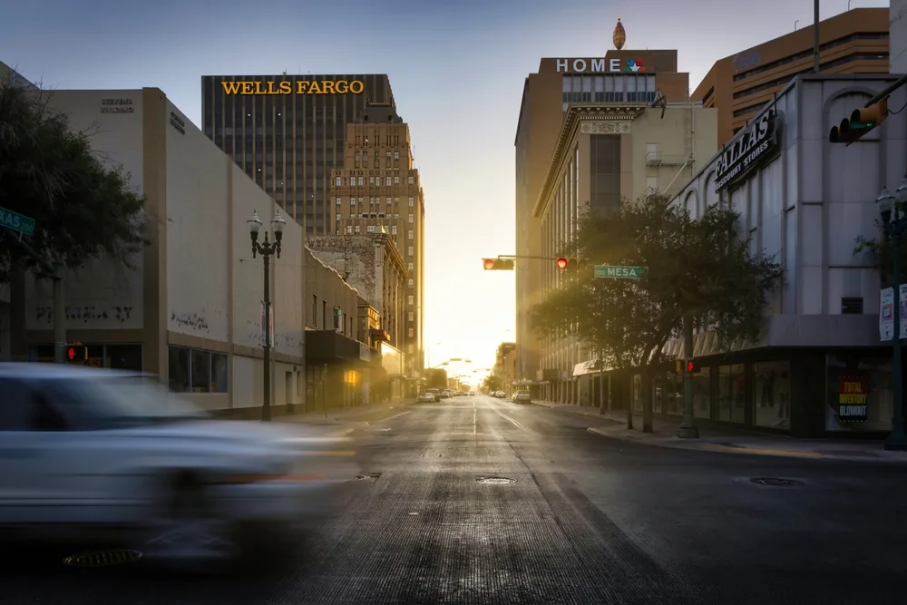 Photo of the sun gleaming through the otherwise dark downtown area in in the intersection of Texas Ave and Mesa Street for a post titled Is El Paso Safe to Visit