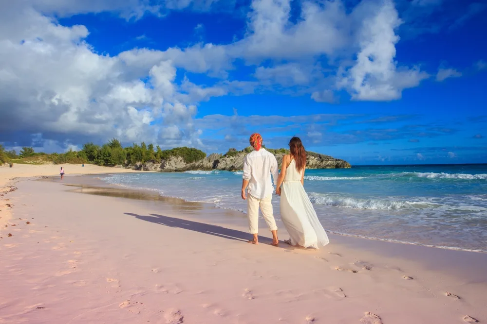 Older couple holding hands and walking along Horseshoe Bay during the best time to visit Bermuda