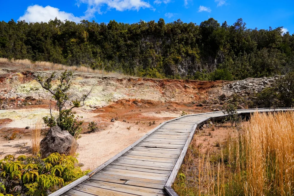 Wooden boardwalk running along a barren sand landscape on the Sulphur Banks Trail pictured for a guide titled the best time to visit Kilauea