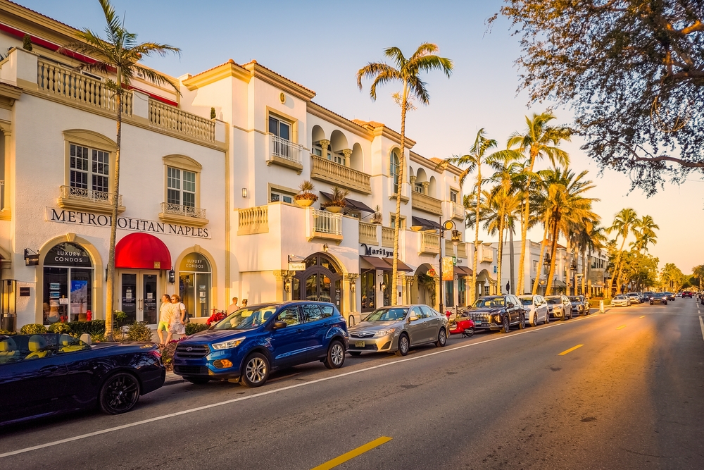 View of 5th Ave at sunset with luxury cars lining the street and palm trees in a neatly-manicured downtown for a guide titled Is Naples Safe to Visit