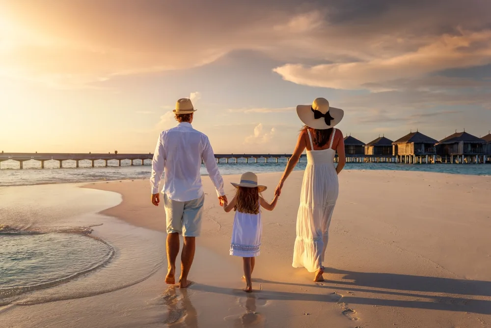 A  sweet family, wearing beach clothes, walking on the beach during sunset, for a piece on a packing guide titled what to wear to the Bahamas.