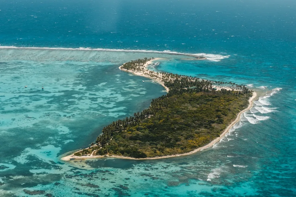 A small private island in the Bahamas where the shore is filled with palm trees and the land area is covered with lush forest, an image for a guide on how many islands are in the region.