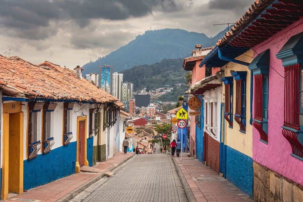 Colorful buildings lining the street in Bogota with a giant mountain the background and a few people walking along