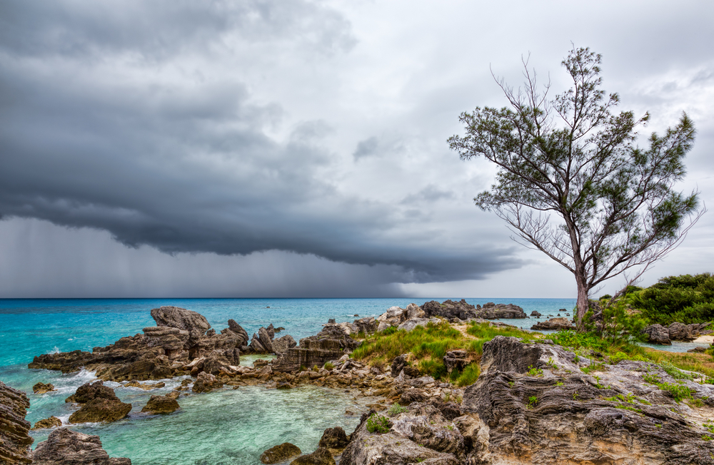 Thunderstorms over Tobacco Bay Beach in Bermuda with a photo of big clouds and rain over the ocean as seen from the green rocky shore