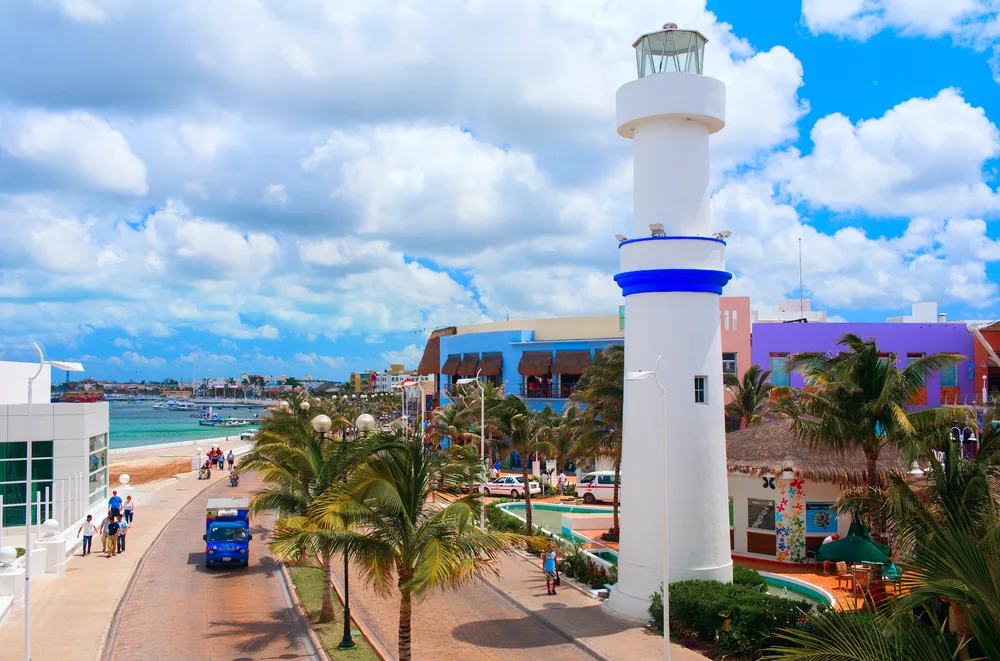 Photo of a lighthouse with a blue stripe towering over a road with cars and trucks going by for a guide titled Is Cozumel Safe to Visit