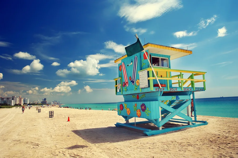 Picturesque photo of a colorful teal and yellow guard shack below a blue sky and next to still water for a guide titled Is Miami Safe to Visit