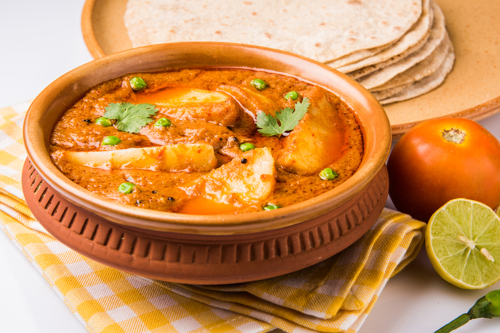 A curry served on a ceramic pot with raw tomato and lime on the table, a taste of Caribbean food.